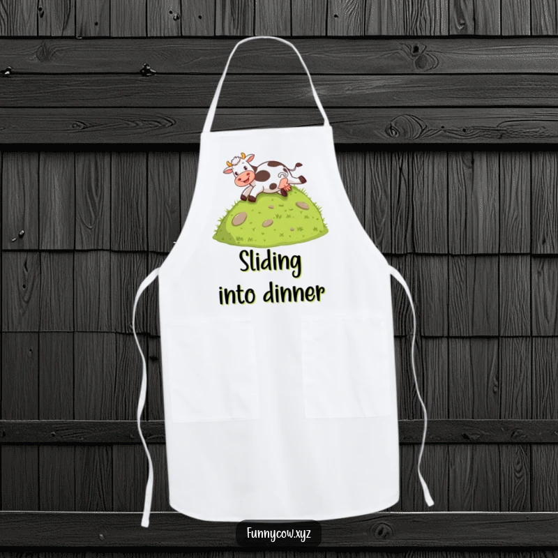 Funny apron showing a cow joyfully sliding down a grassy hill on its behind, ideal for kitchen fun.